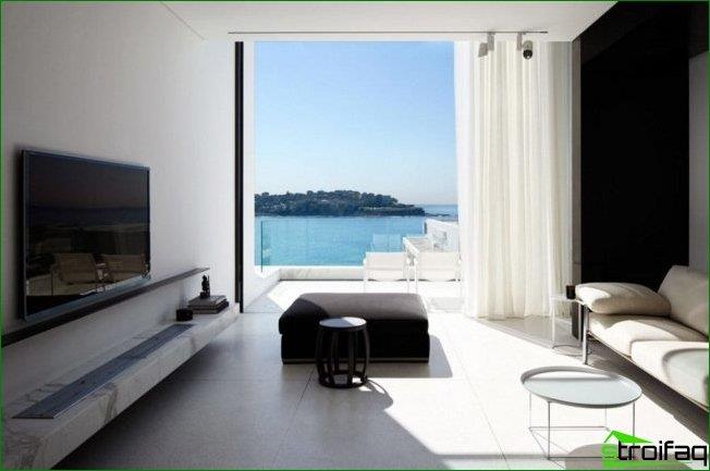 Rummeligt værelse med et minimum af detaljer: en hylde med et tv, et stort vindue, en sofa, et sofabord